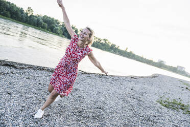 Fröhliche Frau mit ausgestreckten Armen läuft am Flussufer - UUF24002