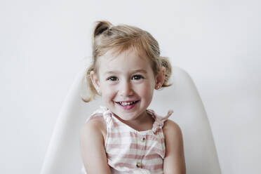 Happy blond girl sitting on chair against white background - EBBF04200