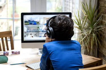 UK, Rear view of boy (10-11) with headphones sitting in front of computer - ISF24715