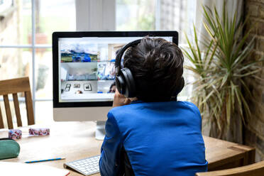 UK, Rückansicht eines Jungen (10-11) mit Kopfhörern, der vor einem Computer sitzt - ISF24715