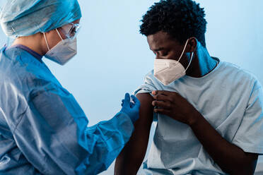 Ärztin in Schutzkleidung und Latexhandschuhen bei der Impfung eines afroamerikanischen Patienten in einer Klinik während des Ausbruchs des Coronavirus - ADSF25598