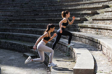 Seitenansicht einer fitten Frau in Sportkleidung, die beim Aufwärmen vor einer Yoga-Sitzung Übungen macht und eine Steintreppe betritt - ADSF25625