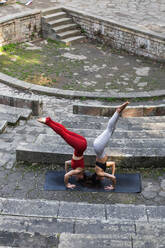 Von oben von fitten Frauen, die in Salamba Sirsasana balancieren, während sie gemeinsam auf einer Matte auf einer Steintreppe Yoga üben - ADSF25626