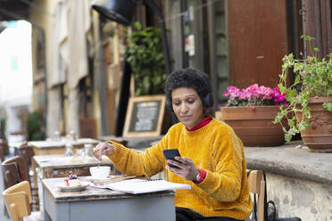 Italien, Toskana, Pistoia, Frau sitzt in einem Café im Freien und benutzt ein Smartphone - ISF24839