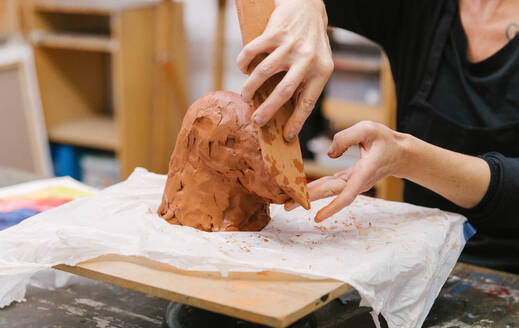 Crop unrecognizable female ceramist using clay and creating handmade earthenware in art studio - ADSF25660