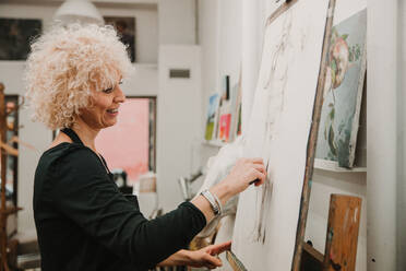 Weibliche Künstlerin zeichnet einen Menschen mit Bleistift, während sie an einer Staffelei im Atelier steht - ADSF25668