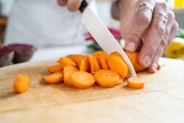 Eine nicht erkennbare Frau schneidet eine rohe Karotte mit einem Messer, während sie ein vegetarisches Essen im Haus zubereitet - ADSF25674