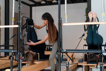 Side view of fit adult female in sportswear doing Three Legged Downward  Facing Dog pose on reformer during Pilates workout in modern gym stock photo