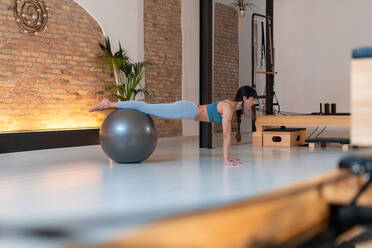 Seitenansicht einer fitten Frau in Sportkleidung bei einer Übung auf einem Fit-Ball während des Trainings im Pilates-Fitnessstudio - ADSF25684