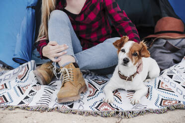 Junge Frau sitzt mit Hund im Zelt beim Camping - EBBF04217