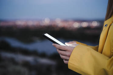 Junge Frau surft in der Abenddämmerung mit ihrem Handy im Internet - EBBF04236