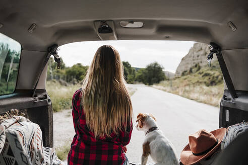 Blonde Frau mit Jack Russell Terrier sitzt im Kofferraum eines Autos - EBBF04250