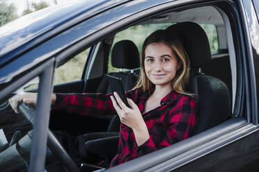 Lächelnde schöne Frau mit Smartphone im Auto sitzend - EBBF04261