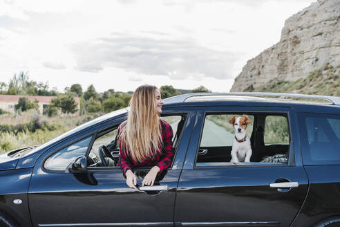 Glückliche junge blonde Frau und Hund am Autofenster - EBBF04262