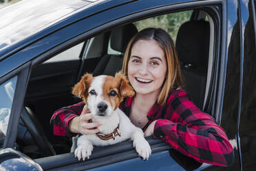 Beautiful happy young woman with dog sitting in car - EBBF04264