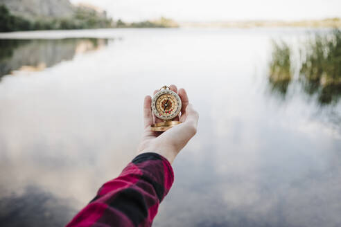 Young woman using navigational compass in front of lake - EBBF04282