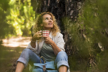 Frau schaut weg, während sie eine Kaffeetasse im Wald hält - SIPF02318