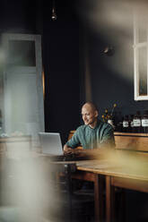 Businessman smiling while using laptop in cafe - GUSF06077