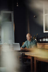 Geschäftsmann lächelnd bei der Benutzung eines Laptops in einem Cafe - GUSF06077