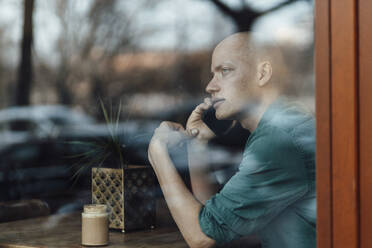 Geschäftsmann schaut durch das Fenster, während er in einem Café mit seinem Handy telefoniert - GUSF06114