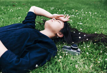 Junge Fotografin mit altmodischer Kamera im Gras liegend - ASGF00796