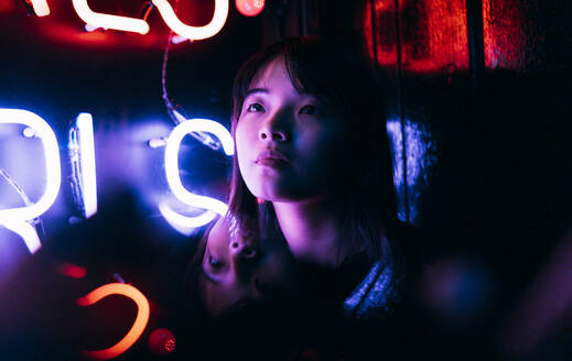 Young woman looking away in front of illuminated neon lighting - ASGF00801