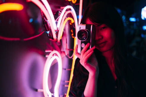 Junge Fotografin beim Fotografieren von Neonlicht mit einer Kamera im Retrostil - ASGF00802