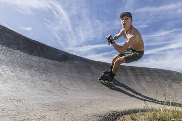 Hemdloser junger Mann beim Rollschuhlaufen im Skateboardpark - STSF02991