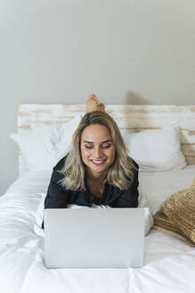 Geschäftsfrau arbeitet am Laptop, während sie zu Hause auf dem Bett liegt - PNAF02033