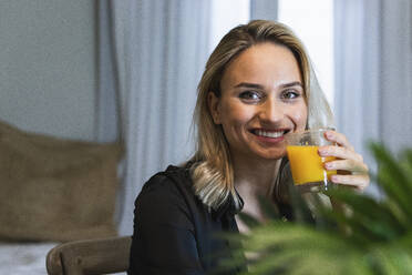 Smiling female professional holding juice glass at home - PNAF02038