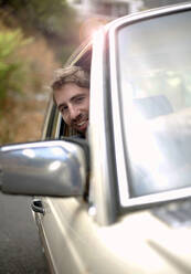 Young man leaning out of car window during road trip - AJOF01525