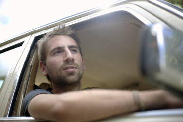 Young man looking through window while driving car - AJOF01528