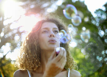 Young woman making bubbles at park - AJOF01538