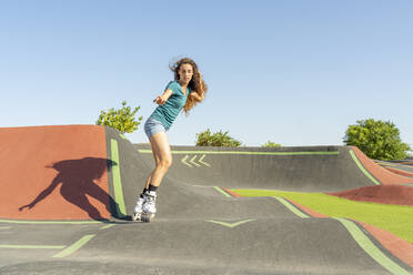 Young woman with hand in hair roller skating on pump track during sunny day - DLTSF02030