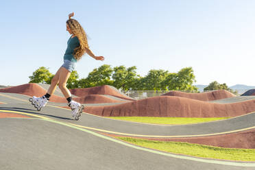 Young woman with brown hair enjoying inline skating at pump track on sunny day - DLTSF02032