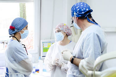 Anonymer männlicher Chirurg mit medizinischem Fernglas spricht mit weiblichen Kollegen in sterilen Masken, während sie sich im Krankenhaus ansehen - ADSF25741