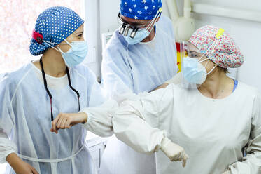 Unkenntlich gemachter männlicher Chirurg mit weiblichen Kollegen in Uniform, die sich bei der Arbeit im Krankenhaus mit einem Ellbogenstoß begrüßen - ADSF25742