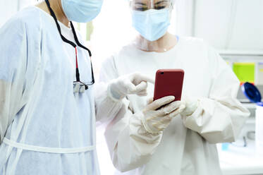 Female surgeons in medical cloth caps surfing internet on cellphone against desktop computer in light hospital - ADSF25744