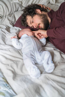 Hoher Winkel des bärtigen Vaters, der ein süßes kleines Kind umarmt, während sie auf einem zerknitterten Bett liegen und sich gegenseitig ansehen - ADSF25769