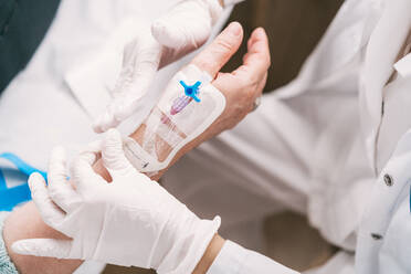 Hohe Winkel der Ernte anonymen Arzt in Einweghandschuhen setzen intravenösen Katheter auf den Arm des Patienten im Krankenhaus - ADSF25784