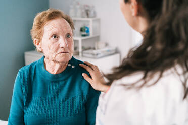 An anonymous doctor comforts a sad elderly woman during a hospital examination, sharing a compassionate moment - ADSF25790