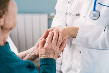 Crop anonymous doctor speaking with elderly woman while holding hands during examination in hospital - ADSF25798