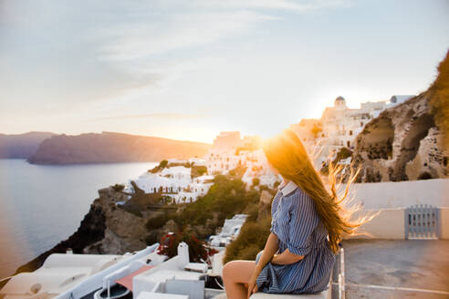 Back view of unrecognizable female traveler admiring Oia Village on Santorini island on windy day in Greece - ADSF25832