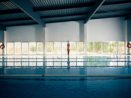 Anonyme weibliche Athletin im Badeanzug steht am Beckenrand gegen reines Wasser mit Bahnen beim Training in einem modernen Gebäude - ADSF25870