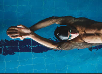 Draufsicht auf einen männlichen Athleten mit Badekappe und erhobenen Armen, der während des Trainings auf dem Rücken schwimmt - ADSF25873