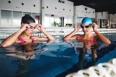 Weibliche Sportlerinnen in Badekappen und Badeanzügen bei der Vorbereitung auf das Training im Schwimmbad mit transparentem Wasser am Tag - ADSF25878