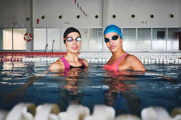 Weibliche Sportlerinnen in Badekappen und Badeanzügen bei der Vorbereitung auf das Training im Schwimmbad mit transparentem Wasser am Tag - ADSF25879
