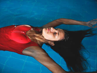 Junge Sportlerin in Badekleidung schwimmt auf dem Rücken in einem Becken mit reinem Wasser und Kräuseln - ADSF25881