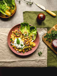 Draufsicht auf appetitliche Kichererbsen mit Burrata-Käse und verschiedenen Gemüsesorten und Kräutern auf einem Teller auf dem Tisch - ADSF25897
