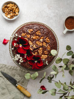 Von oben: süßer Schokoladenkuchen, garniert mit roten Blumen und Walnüssen, serviert auf dem Tisch - ADSF25899